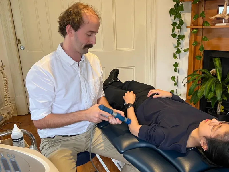 Andrew Macdonald applying a shockwave handpiece to a patient's leg